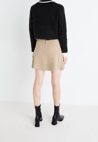 Maglione nero tagliato con bordi bianchi, gonna beige svasata e stivali neri alla caviglia con tacco a blocco, su uno sfondo bianco semplice.