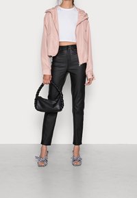 Jasnoróżowa krótka kurtka z elastycznymi mankietami, czarne spodnie z wysokim stanem, czarna pleciona torebka i kratkowane sandały na obcasie z kokardkami.