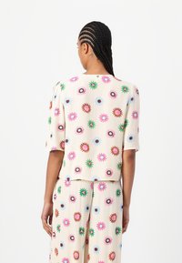 Korte mouwen top in crèmekleurige stof met levendige bloemmotieven in roze, blauw, groen en bruin; losse pasvorm met een ronde halslijn.