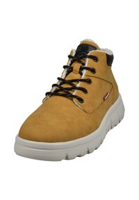 Braune Wildleder-Ankle Boots mit schwarzen Schnürsenkeln, weißem Kunstpelzfutter, gepolstertem Kragen und dicker, weißer, gepolsterter Sohle. Rotes Logo an der Seite.