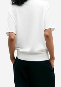 Haut blanc à manches courtes avec ourlet arrondi et poignets côtelés, en tissu doux, assorti à un pantalon foncé ajusté avec poches latérales.