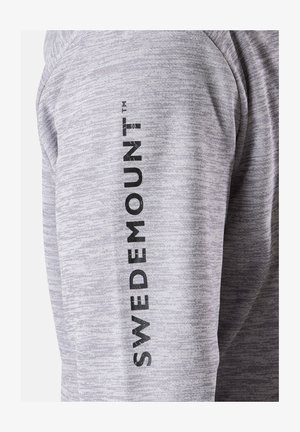 Camicia a maniche lunghe grigia mélange con logo verticale nero "SWEDEMOUNT" lungo il braccio. Il tessuto ha una consistenza liscia.