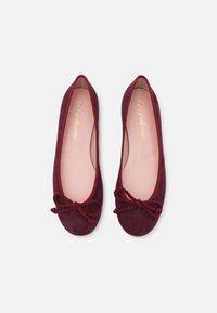 Ballerines en suède bordeaux avec un bout arrondi, une fine doublure beige et un nœud torsadé décoratif à l'avant.