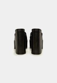Paire de chaussures à plateforme à talons hauts noires vues de dos sur un fond blanc uni.