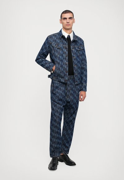 Blaues Denim-Jacken- und Hosen-Set mit einem sich wiederholenden Monogramm-Muster. Komplett mit einem weißen Hemd und schwarzen Schuhen. Glatte Textur.