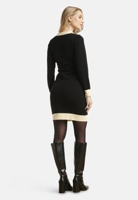 Robe pull noire à manches longues, col et poignets côtelés crème, design ajusté, associée à des bottes en cuir noir montantes.