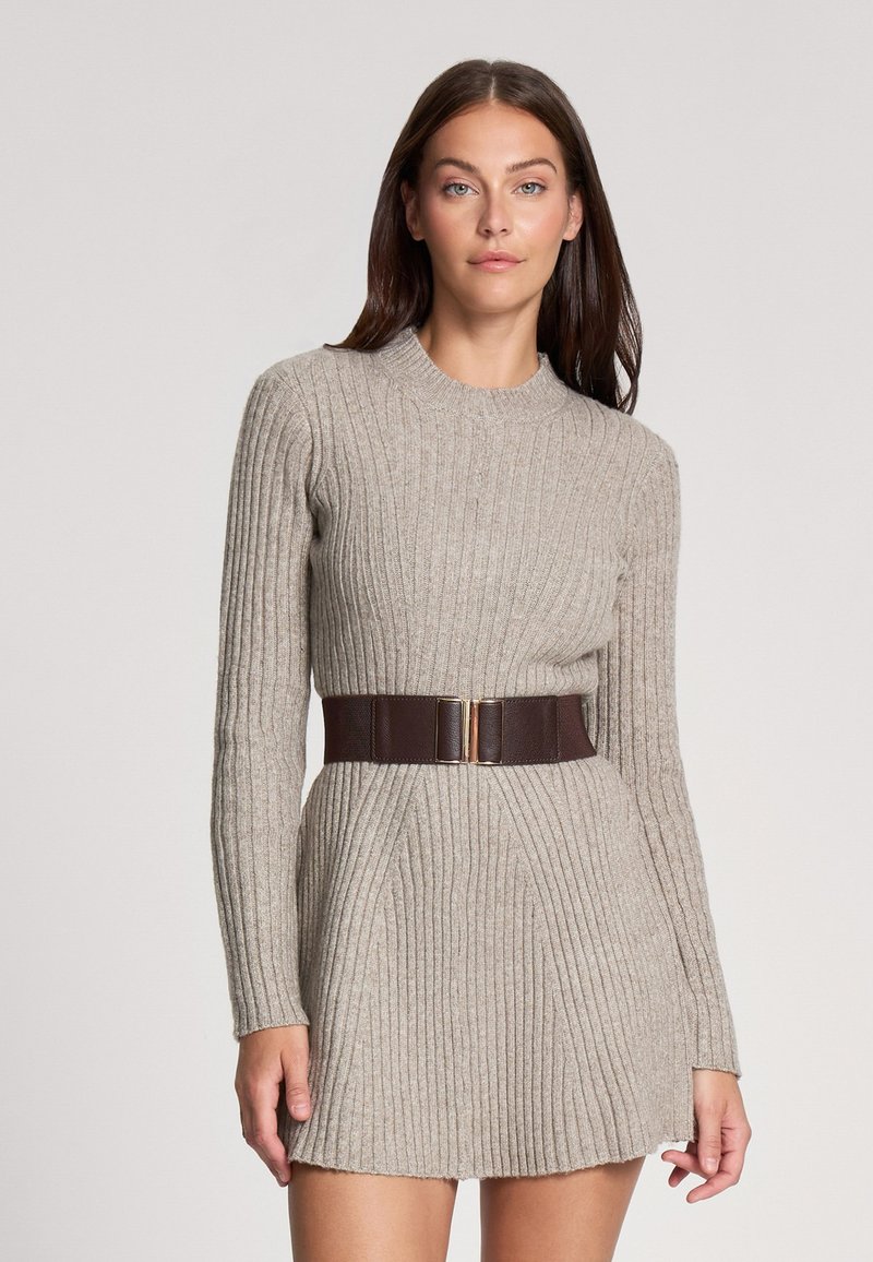 Abito a maglia beige a coste con maniche lunghe, scollatura rotonda e una cintura in pelle marrone con un accentuato fibbia dorata.