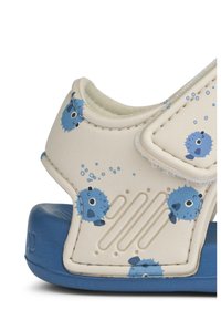 Ανοιχτόχρωμες μπεζ σανδάλες με σχέδια από μπλε ψάρια. Μαλακό, υφασμάτινο επάνω μέρος, ρυθμιζόμενο λουράκι και μπλε λάστιχο στη σόλα με γραμμές για καλύτερη εφαρμογή.