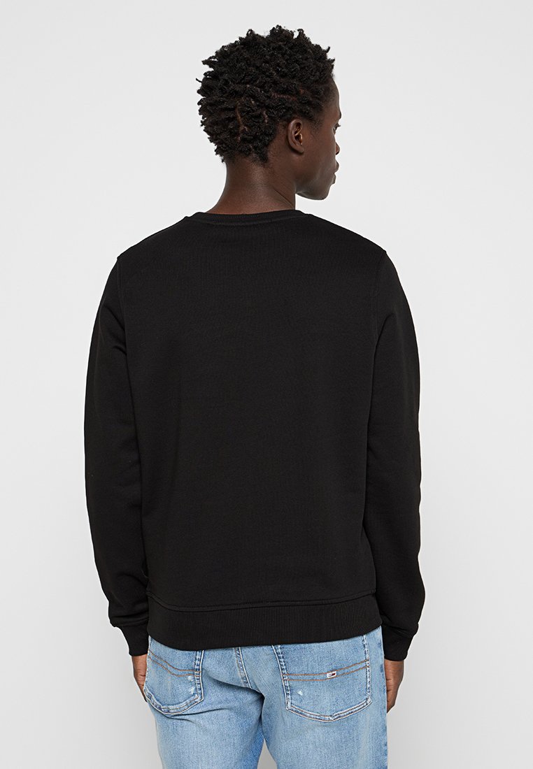 Felpa nera con collo rotondo e polsini a costine. Presenta una texture uniforme, un design aderente ed è abbinata a jeans azzurri chiari.