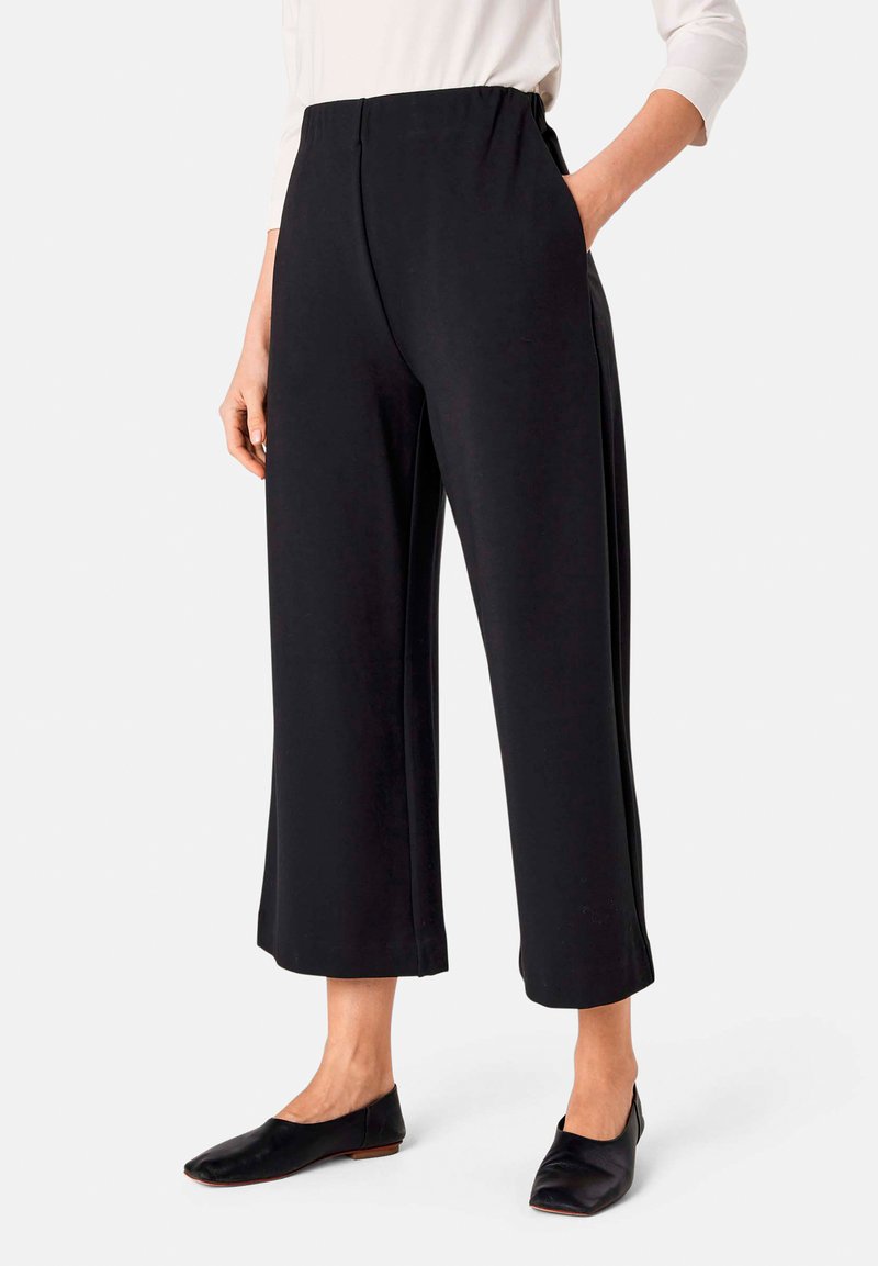 Zwarte wijdvallende broek met een hoge elastische taille, voorzakken, zachte stof en een losse pasvorm. Gepaarde met platte zwarte schoenen.