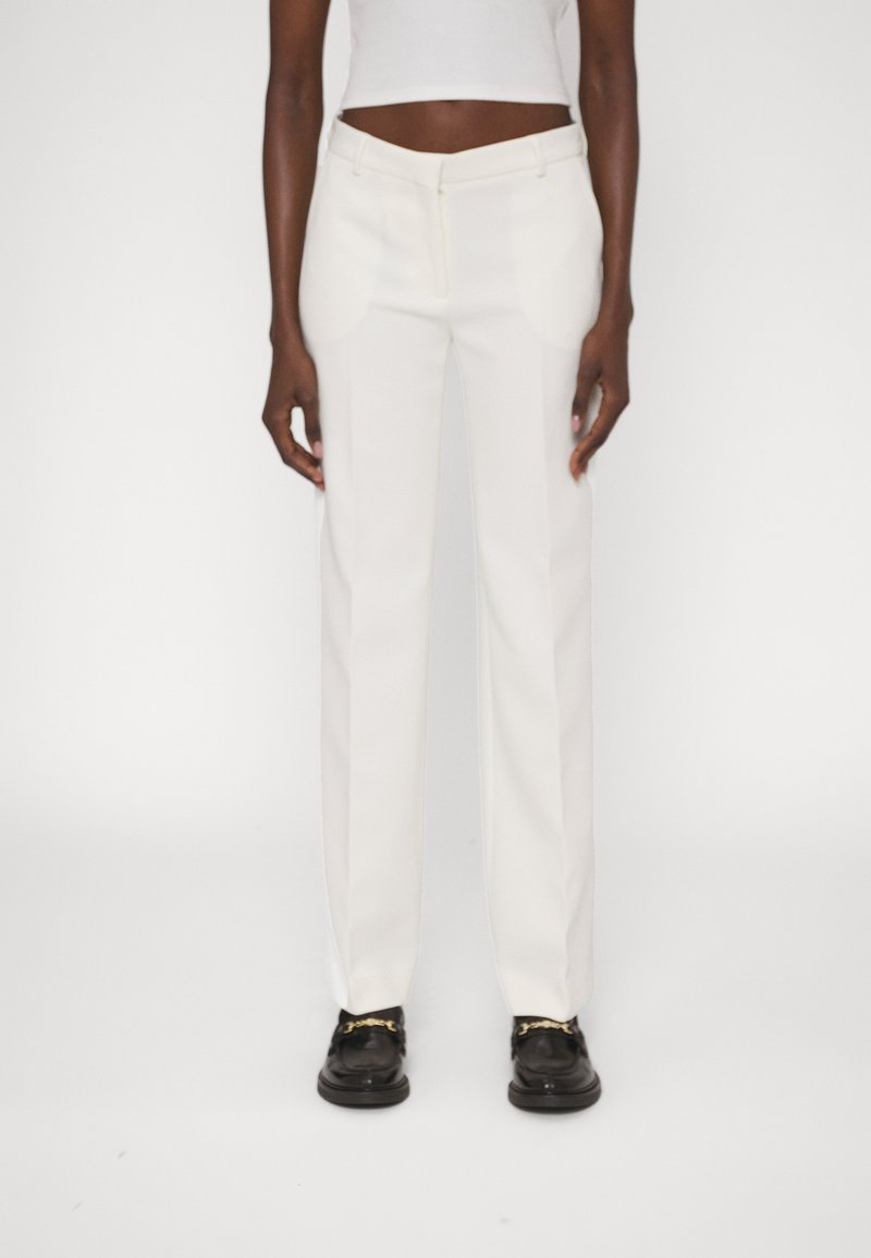 Pantalon blanc ajusté avec une coupe droite, doté de poches latérales et d'un tissu lisse et léger. Associé à des chaussures noires.