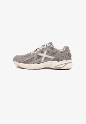 Scarpa da allenamento grigia con tessuto in mesh, dettagli in camoscio, suola bianca ammortizzata e un grande logo bianco sul lato. Design con lacci.