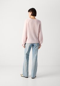 Light pink knit sweater with raglan sleeves and ribbed texture, paired with light blue flared jeans. Minimalist design, plain background.