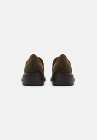 Zapatos de ante verde oliva con suela plana negra, con un diseño minimalista y textura suave, vistos desde la parte posterior.