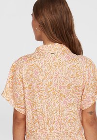 Chemise légère à motifs avec des manches courtes. Présente un design floral dans des tons de rose et d'or, avec une coupe décontractée et un col.