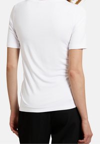 T-shirt bianca a maniche corte con una texture liscia e un collo rotondo, che mostra una silhouette aderente sul retro.