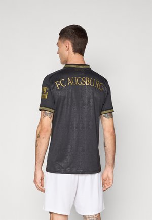 Schwarzes Sporttrikot mit goldenen FC Augsburg Schriftzug, dekorativem Muster, kurzen Ärmeln und einem Kragen. Verfügt über kontrastierende Besätze an den Ärmeln.