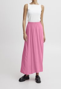 Falda maxi de tejido rosa vivo con cinturilla elástica, combinada con una blusa blanca sin mangas ajustada y zapatos negros de plataforma.