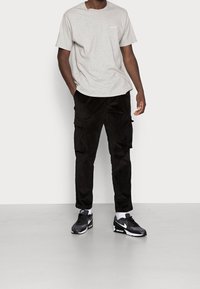 Šedé bavlněné tričko, černé kordové cargo kalhoty s bočními kapsami a černobílé tenisky. Jednoduchý design, uvolněný střih a univerzální barevná paleta.