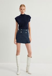 Marineblauwe trui met korte mouwen, gecombineerd met een gestreepte minirok met voorlitsen en zilveren knoopaccenten. Witte kniehoge laarzen.