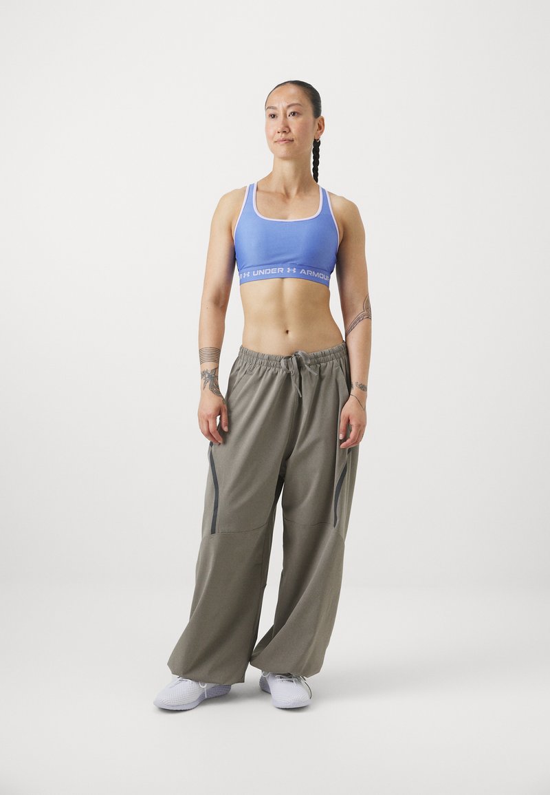 Niebieska sportowa crop top z białym wykończeniem, połączona z luźnymi szarymi dresami z bocznymi zamkami błyskawicznymi oraz białymi butami sportowymi.