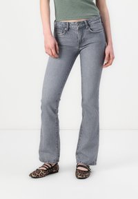 Grå denim flared jeans med fem lommer, frontknapp og glidelås-lukking. Modellen har på seg svarte og leopardmønstrede leiligheter.