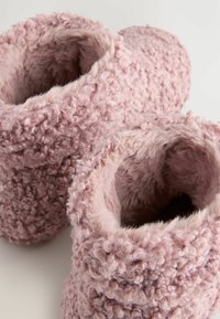 Teksturerede, lyserøde, fnugede tøfler med en blød, plysagtig overflade og runde åbninger. Designet har en fluffet og krøllet stofoverflade.