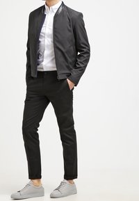 Svart bombarjacka med blank krage, vit skjorta, slim fit svarta byxor och grå sneakers. Snyggt tyg, modern passform.