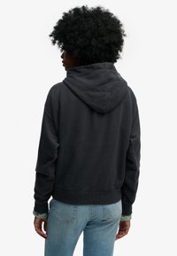 Ciemnoszara bluza z kapturem o luźnym kroju, z prążkowanym ściągaczem u dołu i na rękawach. W połączeniu z jasnoniebieskimi dżinsami, tworząc casualowy wygląd.