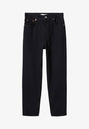 Femme portant une veste en cuir noire, un haut bandeau noir et un jean taille haute noir, fermant la fermeture éclair de la veste sur un fond uni.