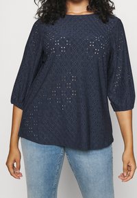 Navy blue, textured blouse with eyelet pattern and three-quarter puff sleeves. Soft cotton fabric and loose fit design for comfort.