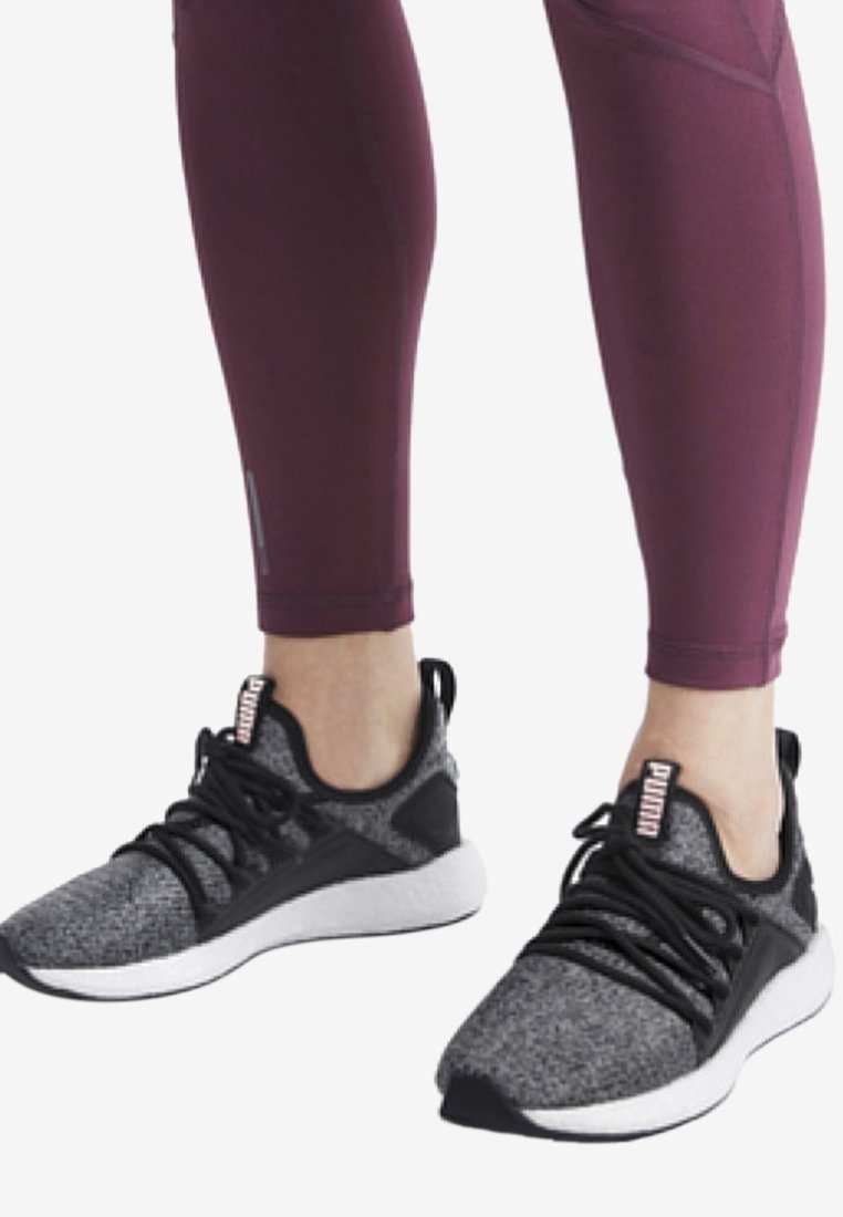 Chaussures de sport noires et grises avec une tige en tricot texturé, lacets plats et semelle blanche, accompagnées de leggings maroon ajustés.