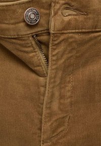 Brown corduroy fabric with visible ribbing, featuring a zipper and a branded metal button at the waistband, alongside a small belt loop detail.