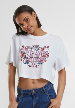 White cropped t-shirt with short sleeves featuring colorful floral and text design in pink and green, showcasing a relaxed fit.