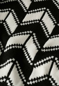Tissu tricoté noir et blanc avec un motif géométrique répétitif de lignes en zigzag inclinées et de formes rectangulaires.