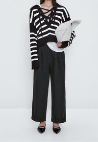 Pull cropped rayé noir et blanc avec un décolleté à lacets, associé à un pantalon large noir et des escarpins noirs à bout pointu.