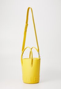 Sac seau en cuir jaune avec deux poignées supérieures, une bandoulière amovible et un lettrage en relief à l'avant. Fini lisse et texturé.