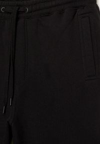Schwarze Sweatpants aus weichem Stoff, mit einem elastischen Bund und verstellbaren Kordeln sowie Seitentaschen. Strukturierte Oberfläche.