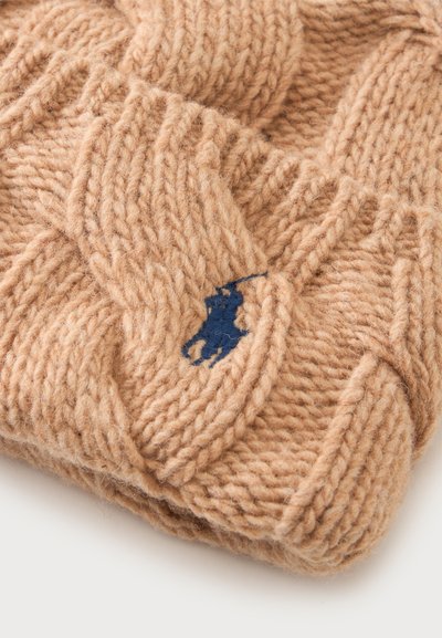 Tissu en laine beige tricoté avec un motif torsadé détaillé et un petit logo brodé bleu marine représentant une personne à cheval.