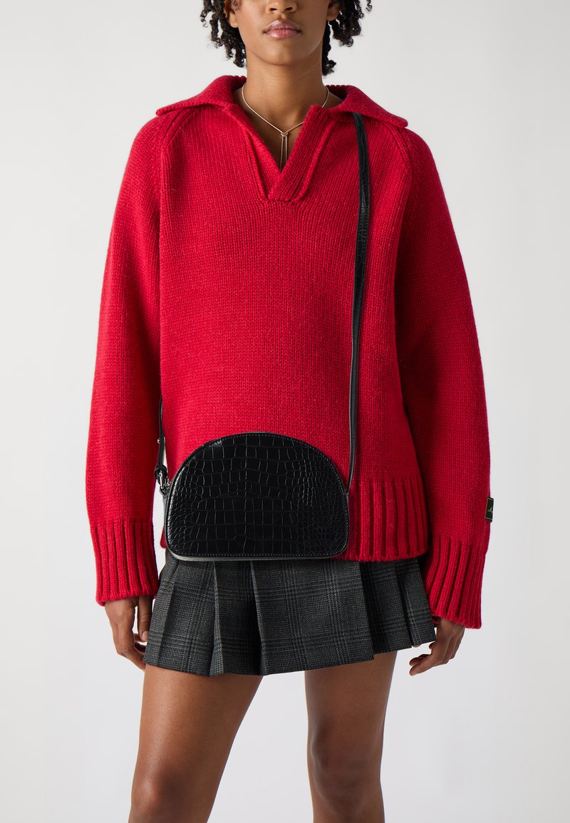 Jersey de punto rojo con cuello, con puños acanalados; bolso bandolera negro con textura de cocodrilo; falda de tablas a cuadros grises.