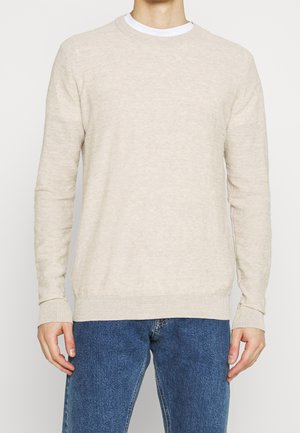 Beige crewneck trui gemaakt van zachte gebreide stof, lange mouwen met geribde manchetten en zoom, gedragen over een witte t-shirt, gecombineerd met blauwe spijkerbroeken.