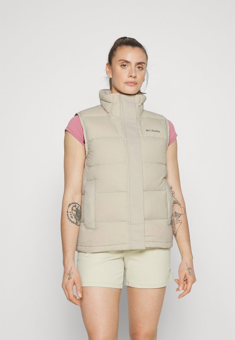 Beige ärmellose Steppweste mit hohem Kragen und gestepptem Design. Gehört zu einem Logo auf der oberen linken Seite und hat seitliche Taschen. Getragen über einem rosa Hemd.