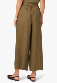 Pantalons amples vert olive avec une finition texturée, taille élastique et longueur raccourcie au niveau de l'ourlet. Portés avec des chaussures à talon ouvert noires.