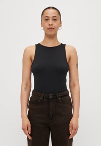 Svart ermeløs bodysuit med rund hals, laget av glatt stoff. Kombinert med mørkebrown høytaljede denimjeans med frontlommer.