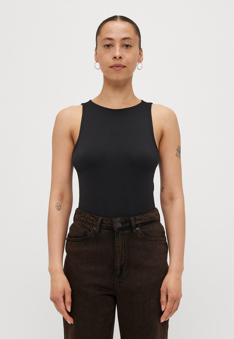 Svart ermeløs bodysuit med rund hals, laget av glatt stoff. Kombinert med mørkebrown høytaljede denimjeans med frontlommer.