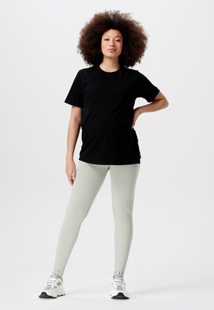 Schwarzes Baumwoll-T-Shirt kombiniert mit hellgrünen Rippleggings. Das Model trägt weiße und graue Sneaker. Einfaches Design und bequemer Sitz.