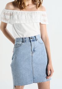 White off-the-shoulder top with lace detailing and a light blue denim mini skirt. Skirt features a front button closure and fringed hem.