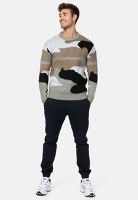 Strikket sweater med camouflage-mønster i beige, grå, hvid og sort. Rund halsudskæring. Kombinationen med mørke bukser og hvide sneakers.