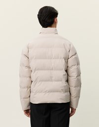Jaqueta puffer bege clara com gola alta, design acolchoado e amplas secções horizontais, feita de um material liso e resistente à água.