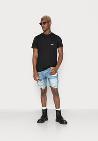 Μαύρο T-shirt με λεπτομέρεια τσέπης, τζιν σορτς με φθορές στις άκρες και μαύρες δερμάτινες μπότες με κορδόνια. Το μοντέλο φορά γυαλιά ηλίου.